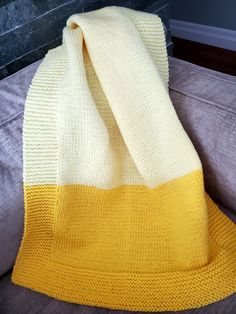 a yellow and white knitted blanket sitting on top of a couch next to a pillow