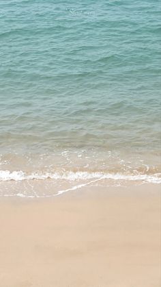 a person walking on the beach with a surfboard in their hand and water behind them