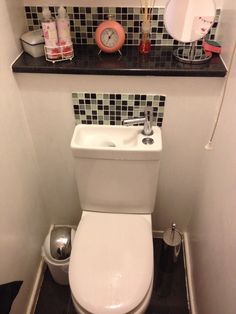 a white toilet sitting in a bathroom next to a sink under a mirror and shelf