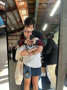 a man and woman standing in front of a mirror looking at their cell phones together