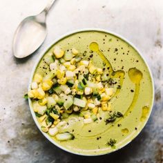 a bowl filled with corn and broccoli on top of a table next to a spoon