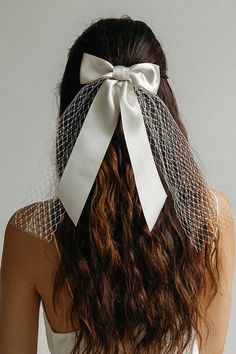 the back of a woman's head wearing a white veil with a bow on it