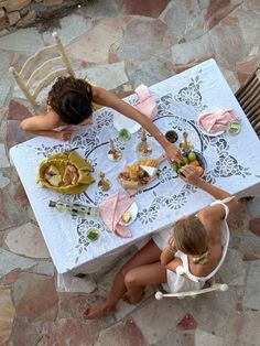 two women sitting at a table with food on it