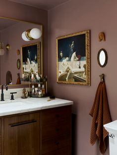 a bathroom with pink walls and gold framed pictures on the wall, along with white counter tops