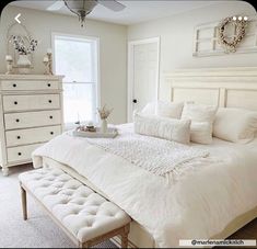 a white bedroom with a large bed and lots of pillows on top of it's headboard