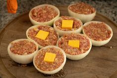 several deviled eggs topped with cheese and meat on a wooden platter, ready to be eaten