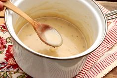 a wooden spoon in a white pot filled with soup on a red and white place mat