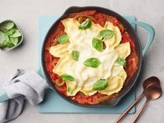 a skillet with ravioli and spinach in it on a blue place mat