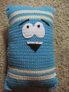 a blue crocheted pillow with a face on it sitting on the floor next to a carpet