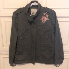 Classic Lightweight Military Style Jacket In Olive (Khaki Green). Pink And Green Embroidered Flowers On The Left Upper Chest And Mid Back. Zipper And Snap Closure With A Soft Stand-Up Collar. Shoulder Epaulettes. Inside Drawstring Waist. Front Upper And Lower Flap Pockets. Smoke Free Home. D99606 Casual Embroidered Long Sleeve Outerwear, Casual Long Sleeve Embroidered Outerwear, Trendy Cotton Outerwear With Floral Embroidery, Trendy Floral Embroidered Long Sleeve Outerwear, Casual Embroidered Fall Outerwear, Casual Long Sleeve Outerwear With Multicolor Embroidery, Long Sleeve Embroidered Outerwear With Pockets, Multicolor Embroidery Long Sleeve Outerwear With Pockets, Casual Floral Embroidery Outerwear For Fall