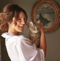 a woman holding a cat in her arms and looking at the camera with a smile on her face