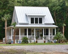 a white house with blue shutters on the front porch and trees in the background