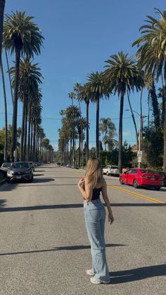 a woman standing in the middle of an empty street with palm trees on both sides