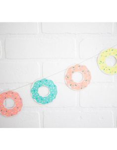 three doughnuts hanging on a string against a white brick wall, one with sprinkles