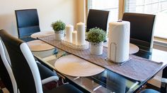 a glass dining table with black chairs and white vases on top of it in front of a window