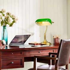 a laptop computer sitting on top of a wooden desk next to a lamp and chair