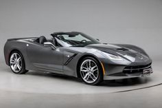 a gray sports car is parked in a room with grey walls and white flooring