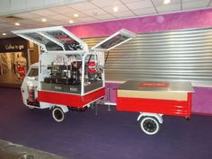 a red and white cart parked in front of a metal building with purple carpeting