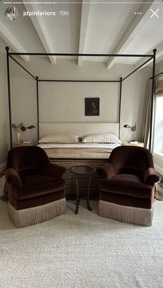 two chairs sitting in front of a bed with an iron frame and canopy over it