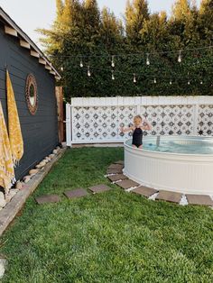 an outdoor hot tub in the backyard next to a fence and grass area with stepping stones