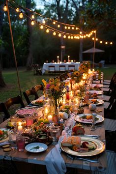 an outdoor dinner table set up with candles, plates and food on it for guests to enjoy