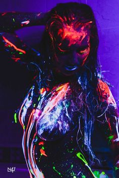 a woman covered in neon paint with her hands on her head and arms behind her back