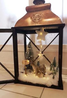 a lighted lantern with deer and christmas trees in the snow, on top of a tile floor