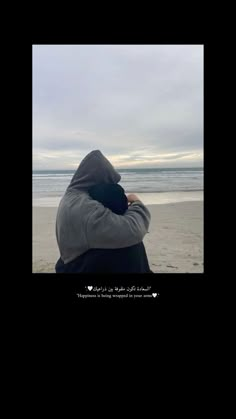 a person sitting on top of a beach next to the ocean with their arms around each other