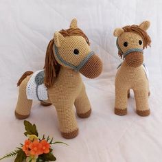 two crocheted stuffed horses sitting next to each other on a white surface with flowers