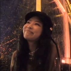 a woman wearing a black hat standing next to a fire hydrant and looking up at the sky