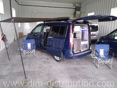 a blue van parked in a garage next to two chairs and an awning over it