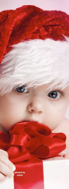 a baby wearing a santa hat and holding a red ribbon over its mouth with the caption, christmas by lolo