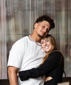 a man and woman hugging each other in front of a wall with glass panels behind them