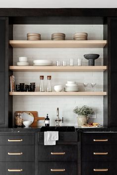 a kitchen with black cabinets and shelves filled with white plates, bowls and other items