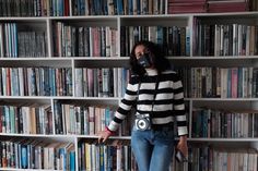 a woman standing in front of a bookshelf with a camera around her neck