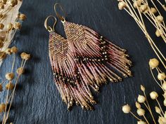 a pair of beaded earrings sitting on top of a black surface next to dried flowers