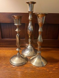 three silver candlesticks sitting on top of a wooden table