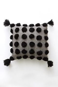 a black and white polka dot pillow with tassels on the front, sitting on a white surface