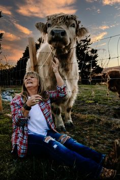 a woman sitting on the ground next to a cow behind a fence with her hands up