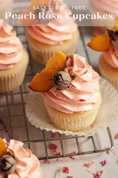 cupcakes with pink frosting and peaches on top are sitting on a cooling rack