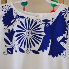 a white shirt with blue and green designs on the front, hanging from a wooden hanger