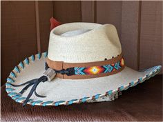 The Nelle starts with a Mexican soft palm leaf hat body that has a 3 3/4" brim and 5 1/4" crown. Hand laced in saddle and turquoise leather lace. The beaded hatband has colors of turquoise and orange and is mounted on tan suede. The back of the band has a deer antler bead for accent. Copper patina Concho and an orange decorative feather completes the hat. Note: Please allow 3-4 weeks. Western Hat Bands With Flat Crown For Beach, Southwestern Flat Brim Hat Bands For Vacation, Natural Bohemian Hats For Western-themed Events, Western Natural Hat Bands For Festivals, Natural Western Hat Bands For Festival, Western Style Natural Hat Bands For Festivals, Southwestern Turquoise Hat With Short Brim, Brown Toquilla Straw Hat Band For Western-themed Events, Handmade Traditional Hat Band For Western-themed Events