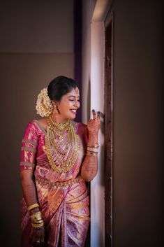 a woman in a pink and gold sari is holding her hand up to the door