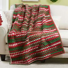 a red and green blanket sitting on top of a couch next to a white chair