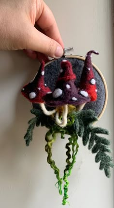 a hand is holding a small felt mushroom ornament on a plant with leaves