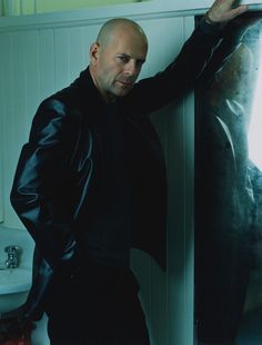 a bald man leaning against a wall with his hand on the glass door and looking at something