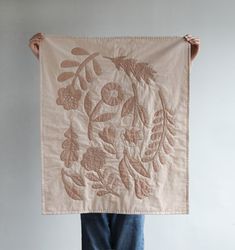 a person holding up a piece of cloth with leaves and flowers on it in front of a white wall