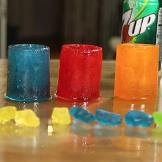 three different colored gummy bears sitting on top of a table next to a can of soda