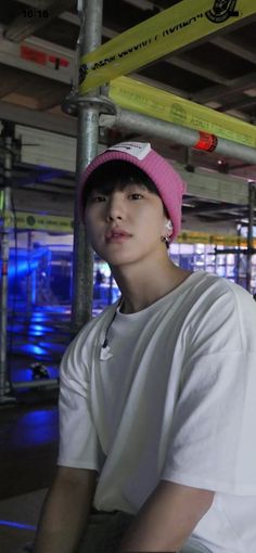 a young man wearing a pink hat sitting on top of a metal pole in a parking garage