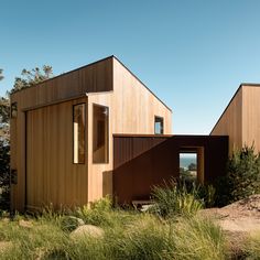 two wooden buildings sitting next to each other on top of a grass covered hillside with trees in the background